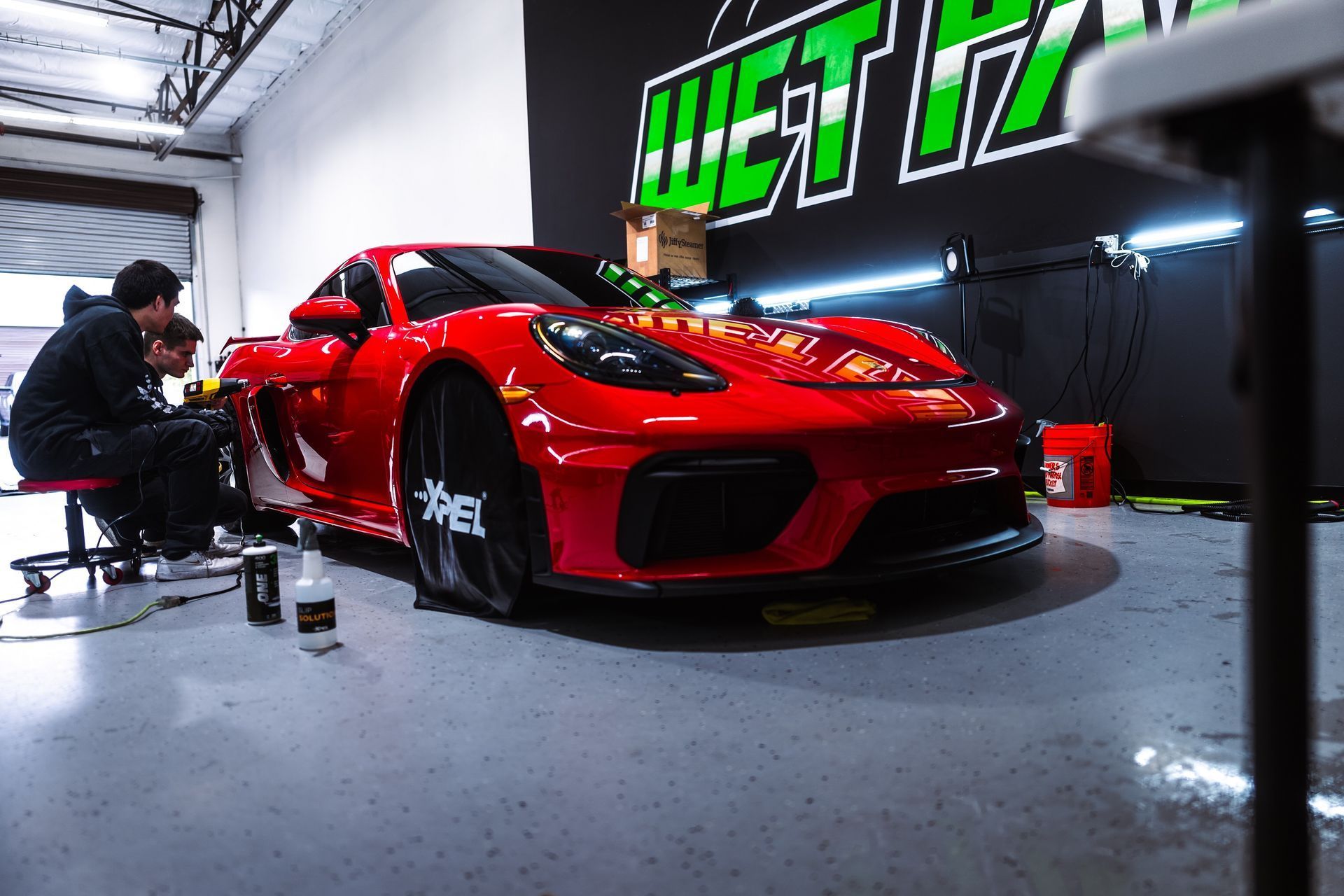 Two men are working on a red sports car in a garage.