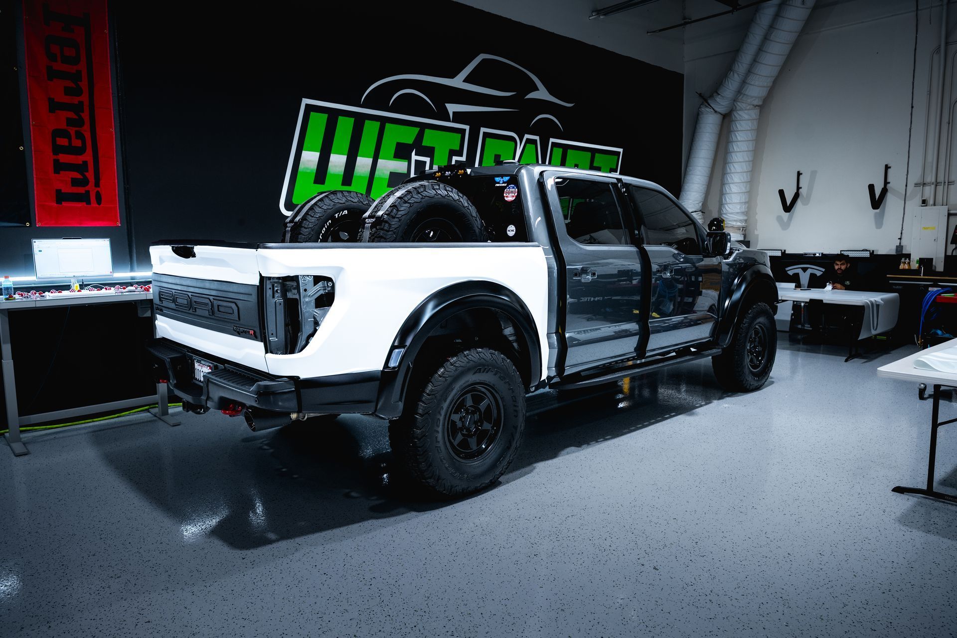 Ford Raptor truck in a garage; white bed, black body, spare tires.