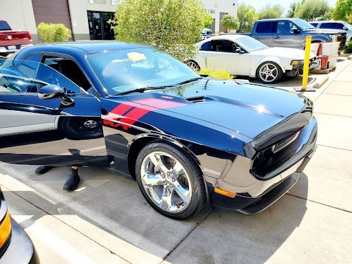 Black sports car with red stripe parked outdoors at a car meet, door open, with other cars nearby
