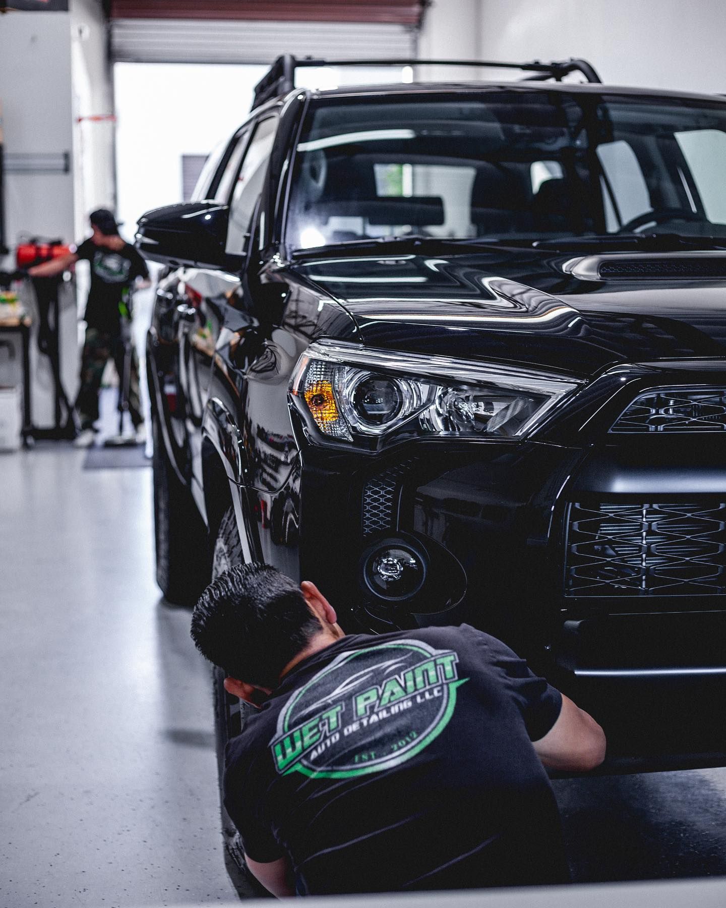 A man is working on a black car in a garage.