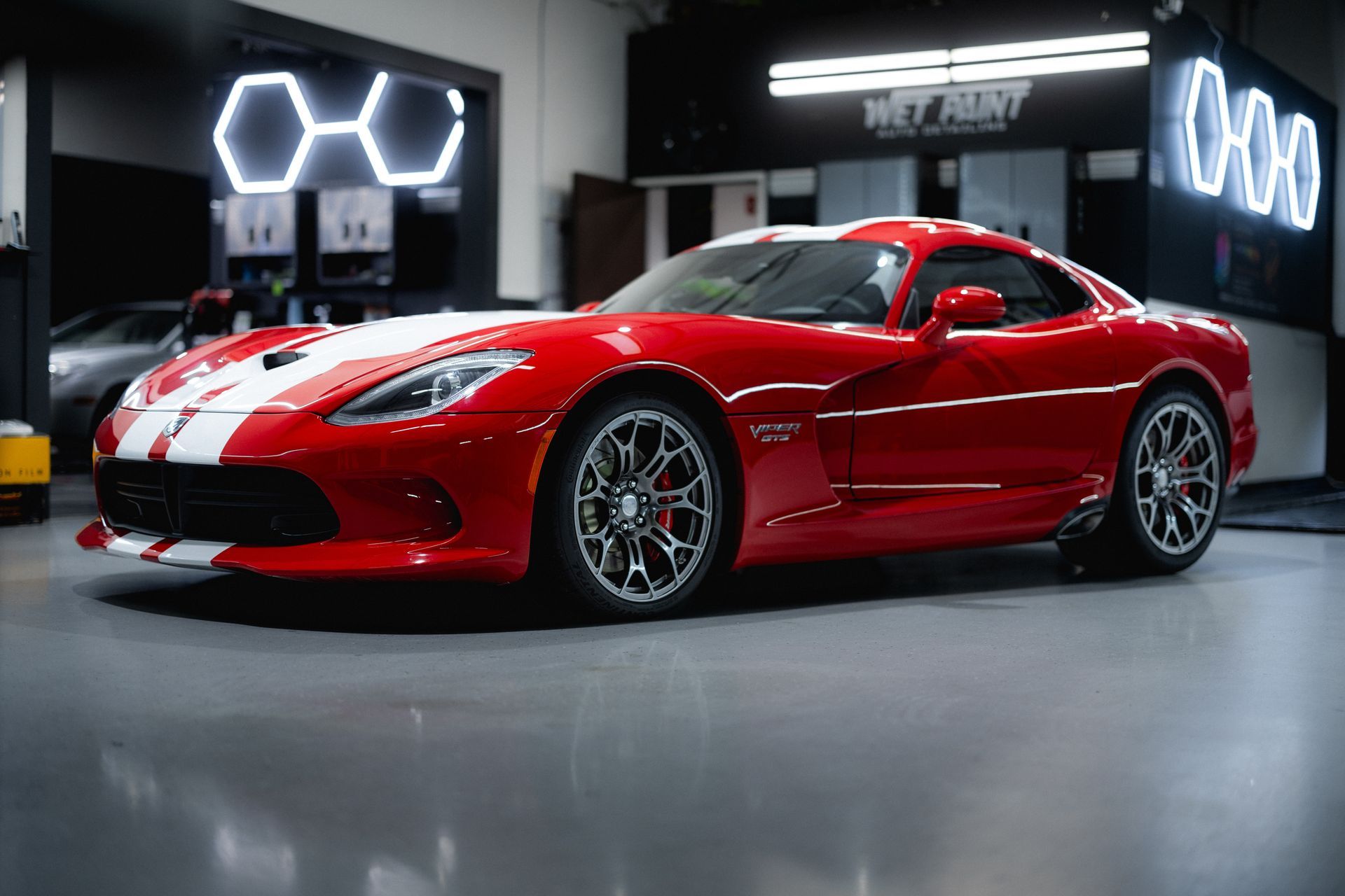 Red Dodge Viper sports car with white racing stripes inside a garage.