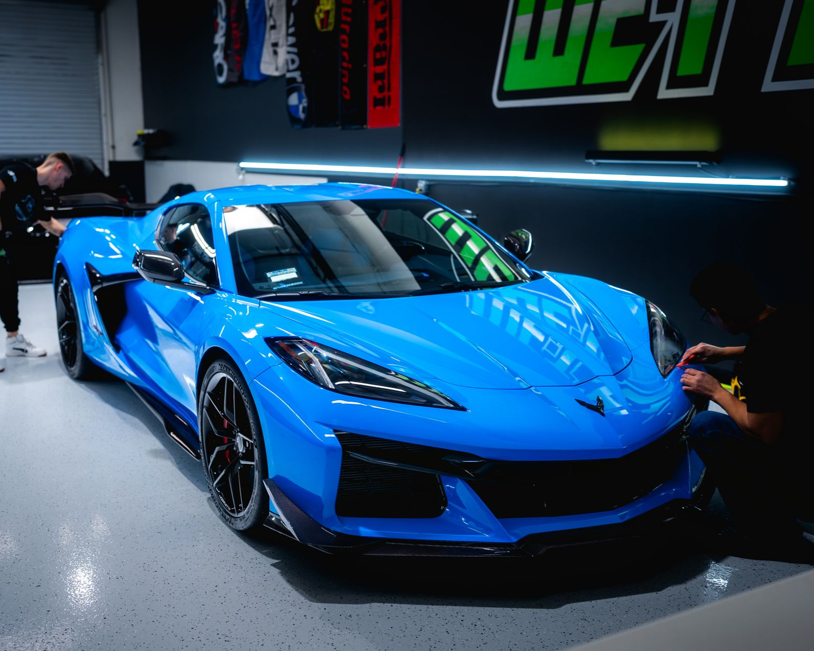 Bright blue sports car in a garage with people working on it.