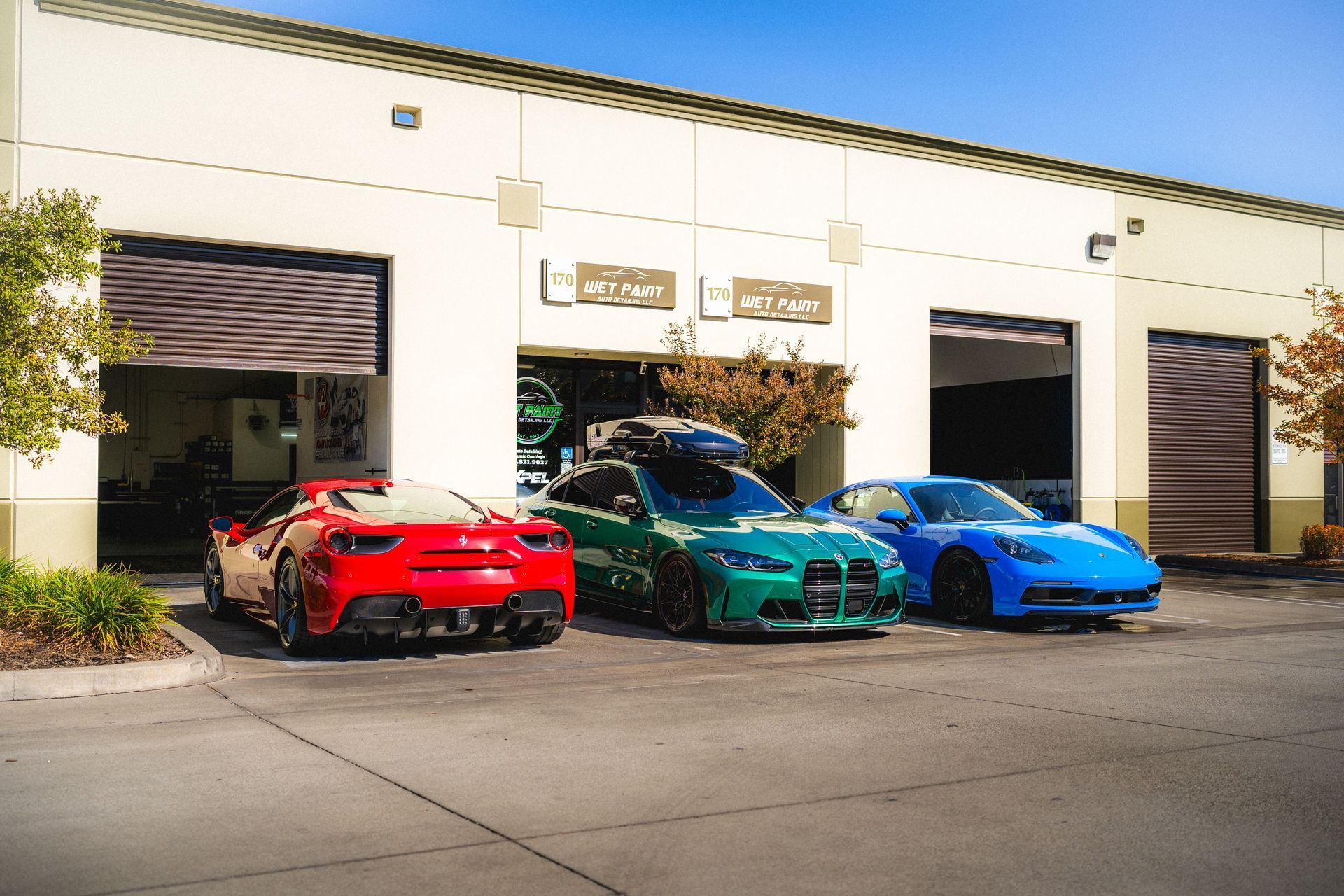 Three sports cars parked in front of a garage: red Ferrari, green BMW, and blue Corvette.