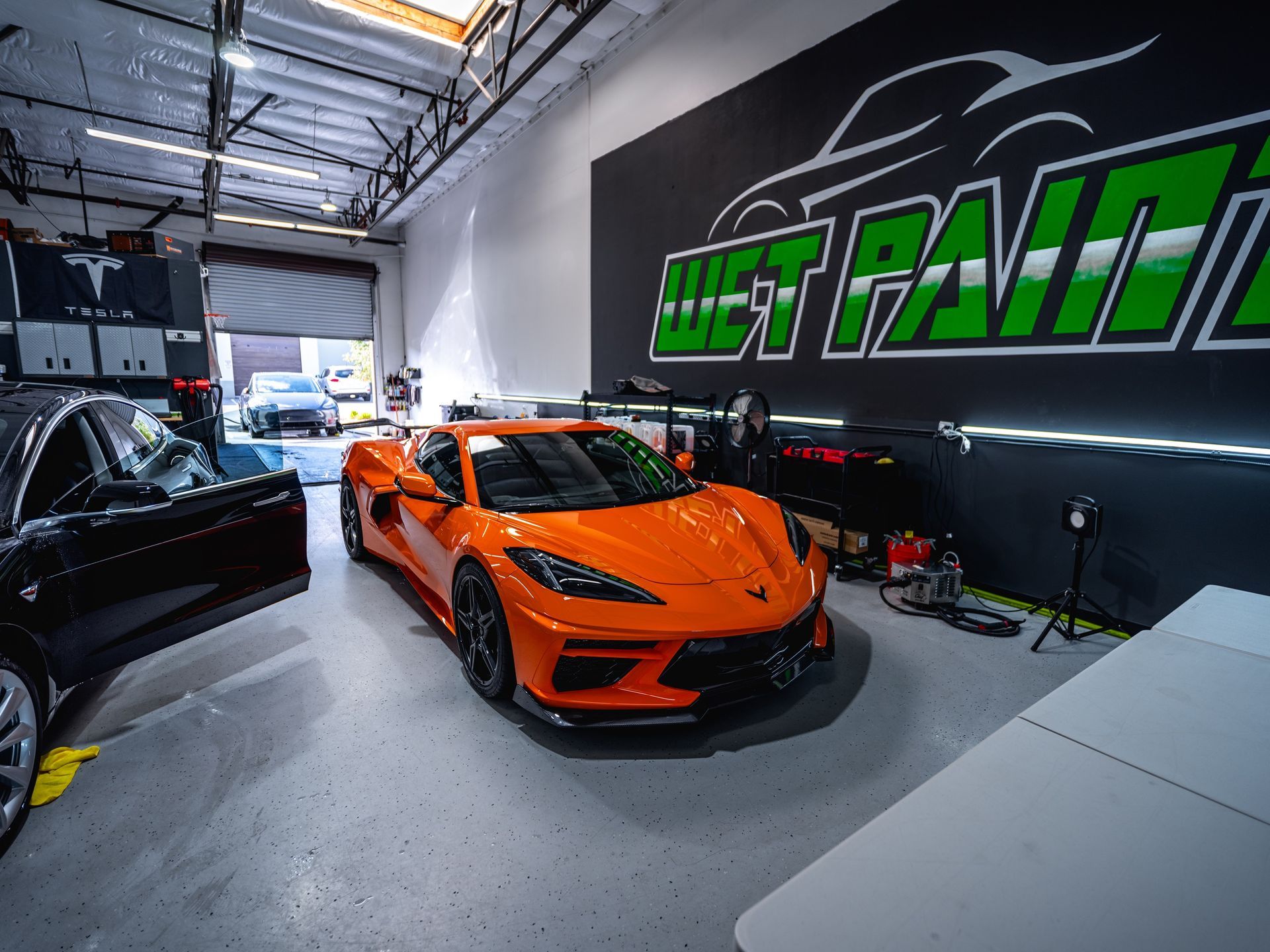 An orange sports car is parked in a garage next to a black car.