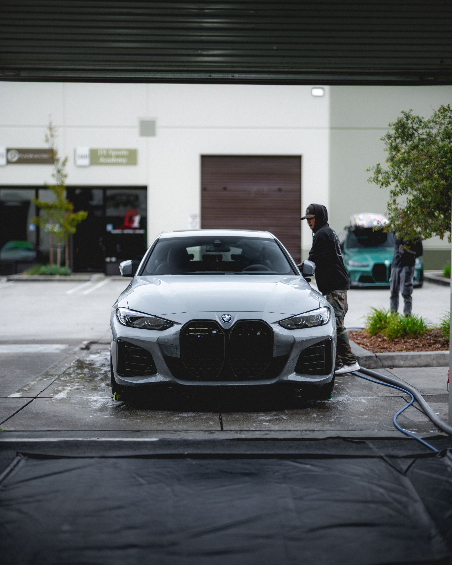 Gray BMW car being washed; person spraying water. Garage setting with two other vehicles.