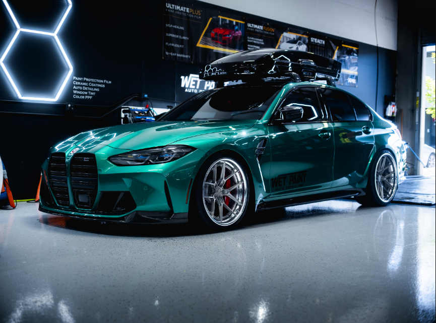 Green BMW sedan with roof cargo carrier, low profile tires, indoors with neon light.