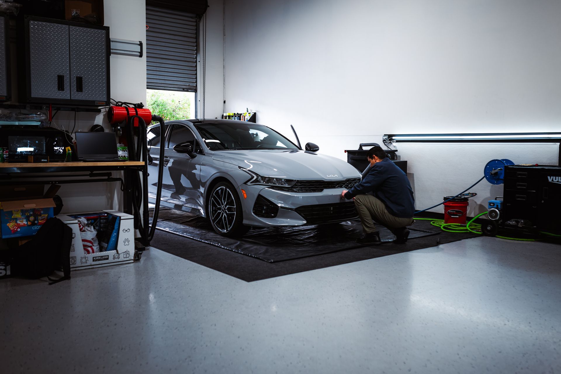 A person washes a gray car inside a well-lit garage.