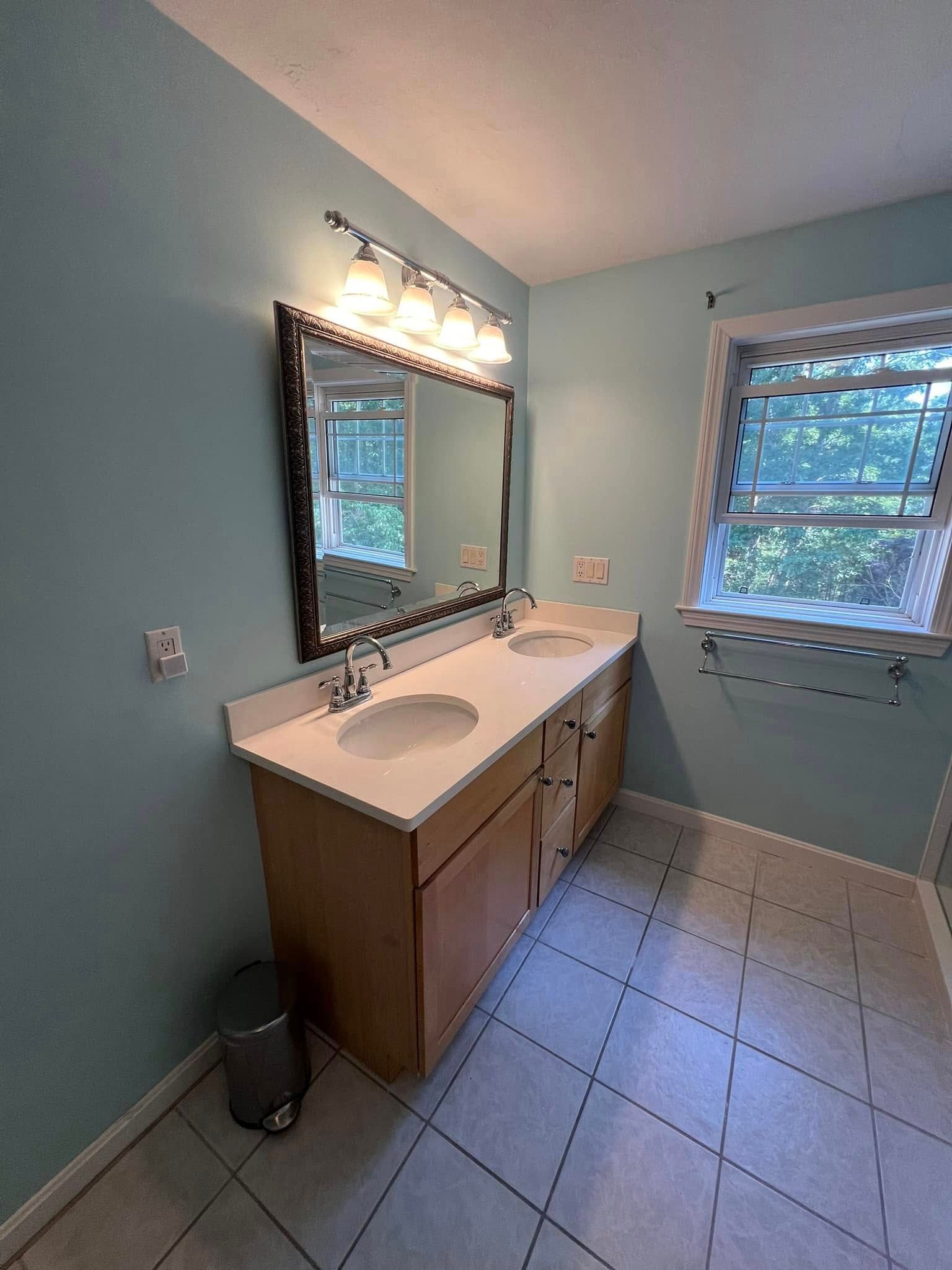 Bathroom with double sink vanity, light blue walls, and a window.