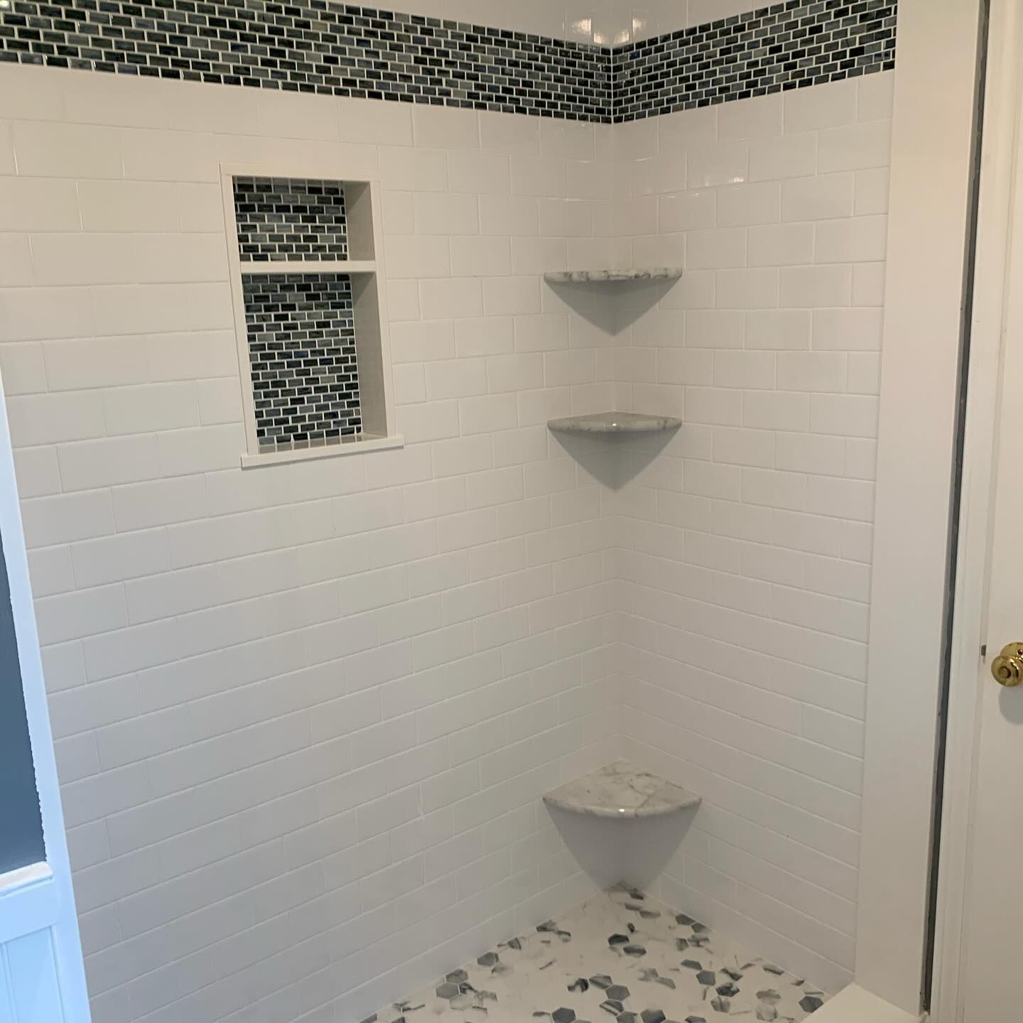 White-tiled shower with black accent tile and built-in shelves. Corner shelves and pebble floor.