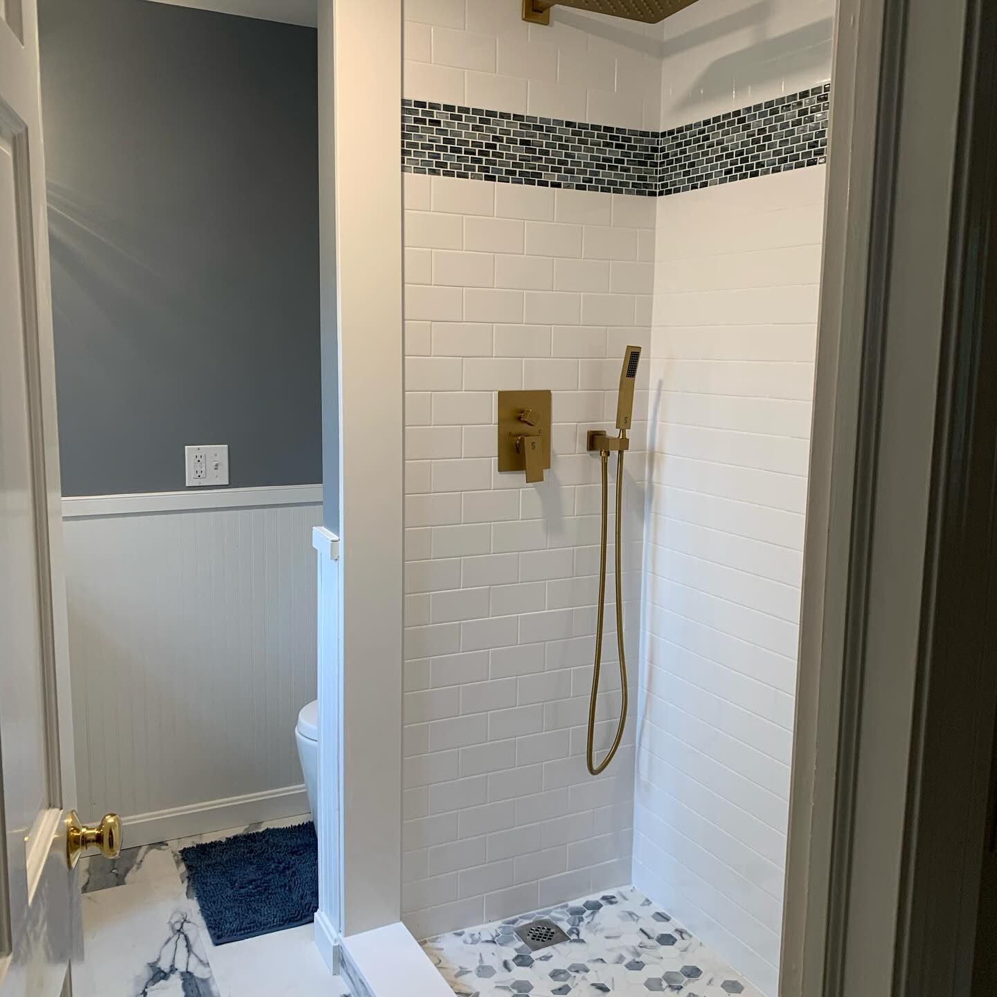 Bathroom with tiled shower, white brick walls, blue and white mosaic tile, gold fixtures.