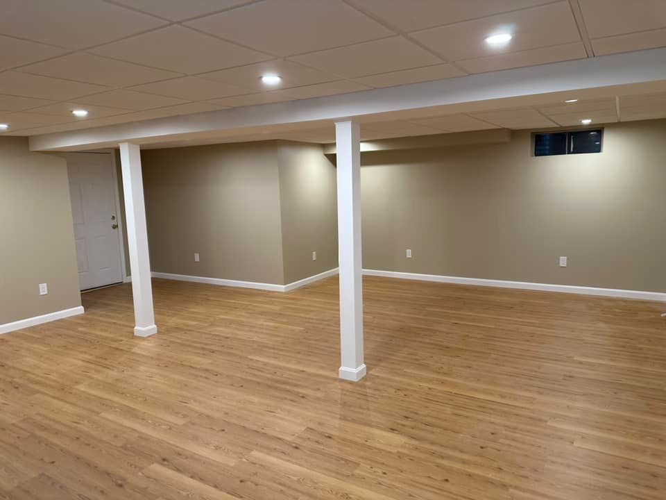 A finished basement with tan walls, hardwood floors, white columns, and recessed lighting.