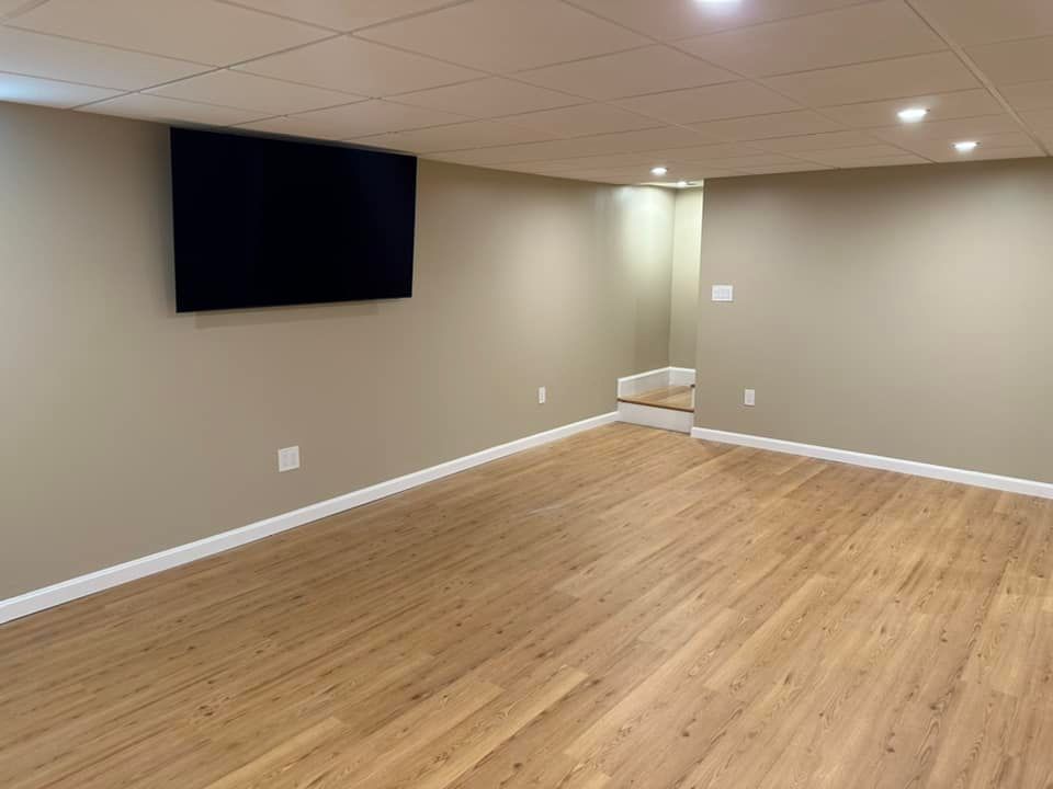 Empty basement with wood-look floor, beige walls, a mounted TV, and recessed lighting.