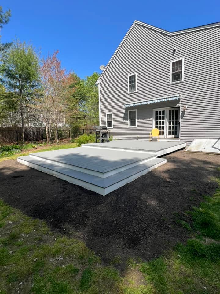 Gray composite deck with white trim attached to a house, surrounded by dirt and grass.