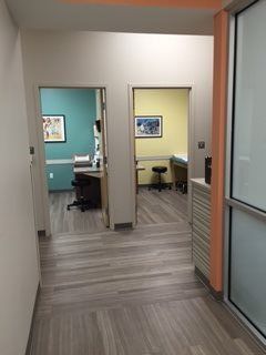 Hallway with two open examination room doors; one teal, the other yellow. Both have artwork and medical equipment.