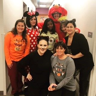 A group of people in Halloween costumes gathered in a hallway. Costumes include Minnie Mouse, Elmo, a cat, and 