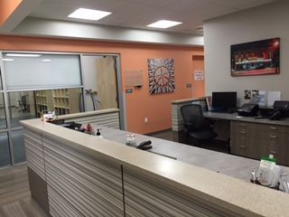 A modern office reception area featuring a light-colored countertop, orange wall, a black desk chair, and a peace sign art.