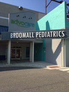 Entrance to Advocare Broomall Pediatrics building; teal and gray exterior, glass doors, sign reading 