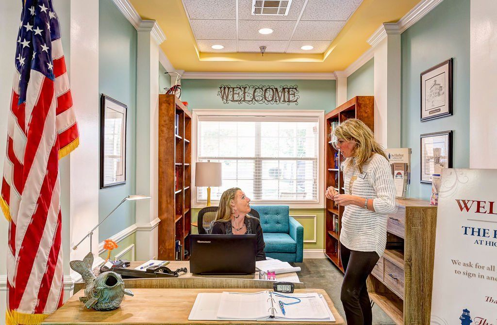 A woman is standing next to a woman sitting at a desk with a laptop.