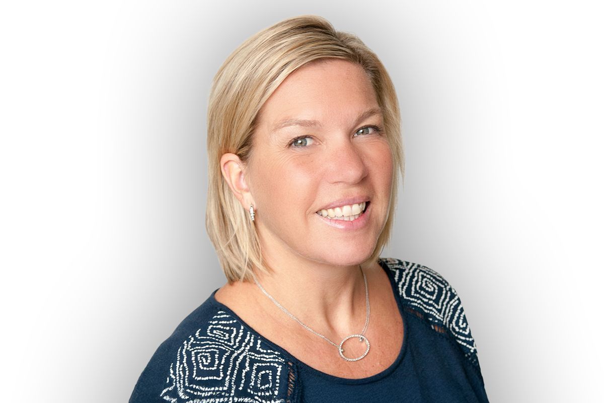 Woman,  Larissa Kostal,  with blonde hair smiles, wearing a patterned blue shirt, silver necklace. 