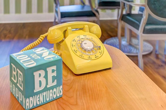 A yellow telephone is sitting on a wooden table next to a block that says be adventurous.