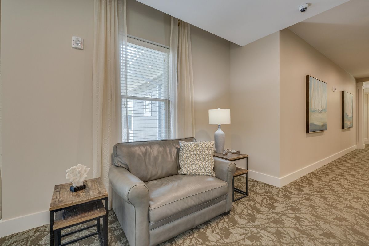 A living room with a chair , table , lamp and window.