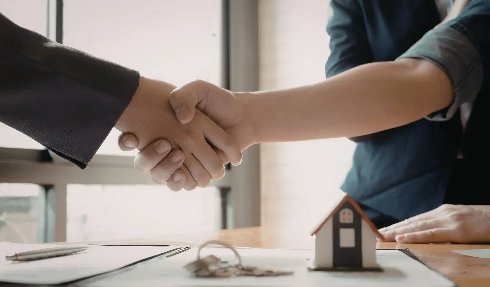 Two people shaking hands over a table with keys and a miniature house.