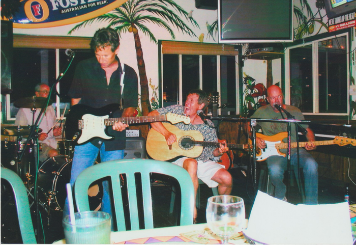 A group of men are playing guitars in front of a sign that says fosters