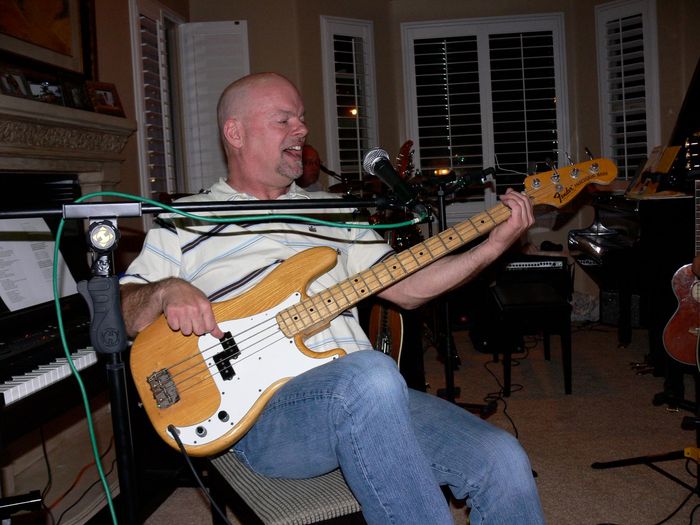 A man is sitting in a chair playing a bass guitar