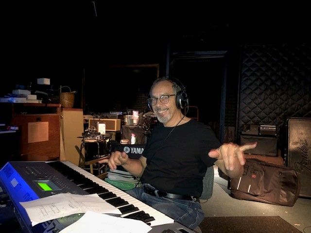 A man wearing headphones is playing a keyboard in a dark room