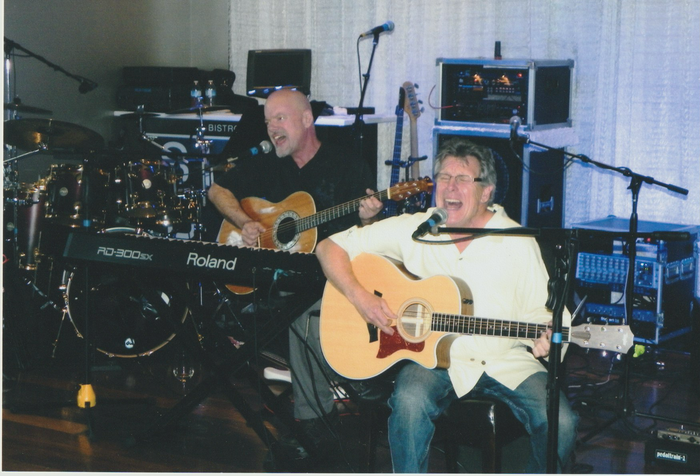 Two men playing guitars in front of a roland keyboard