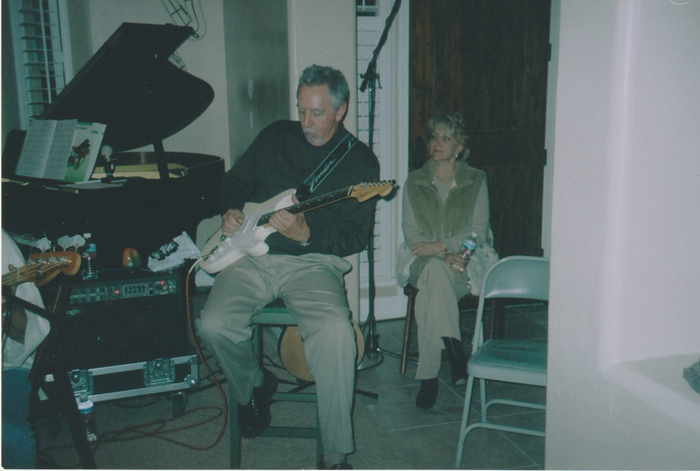 A man is playing a guitar in front of a piano