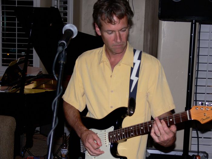 A man in a yellow shirt is playing a guitar in front of a microphone