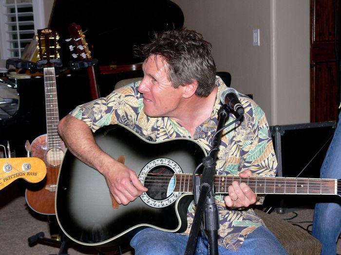 A man in a hawaiian shirt is playing an acoustic guitar