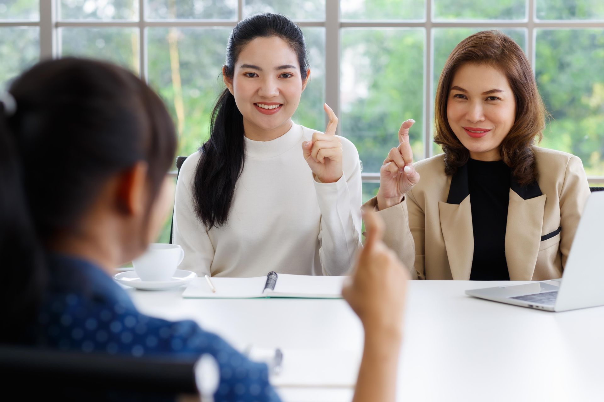 Two Asian women in an interview setting, smiling and signing