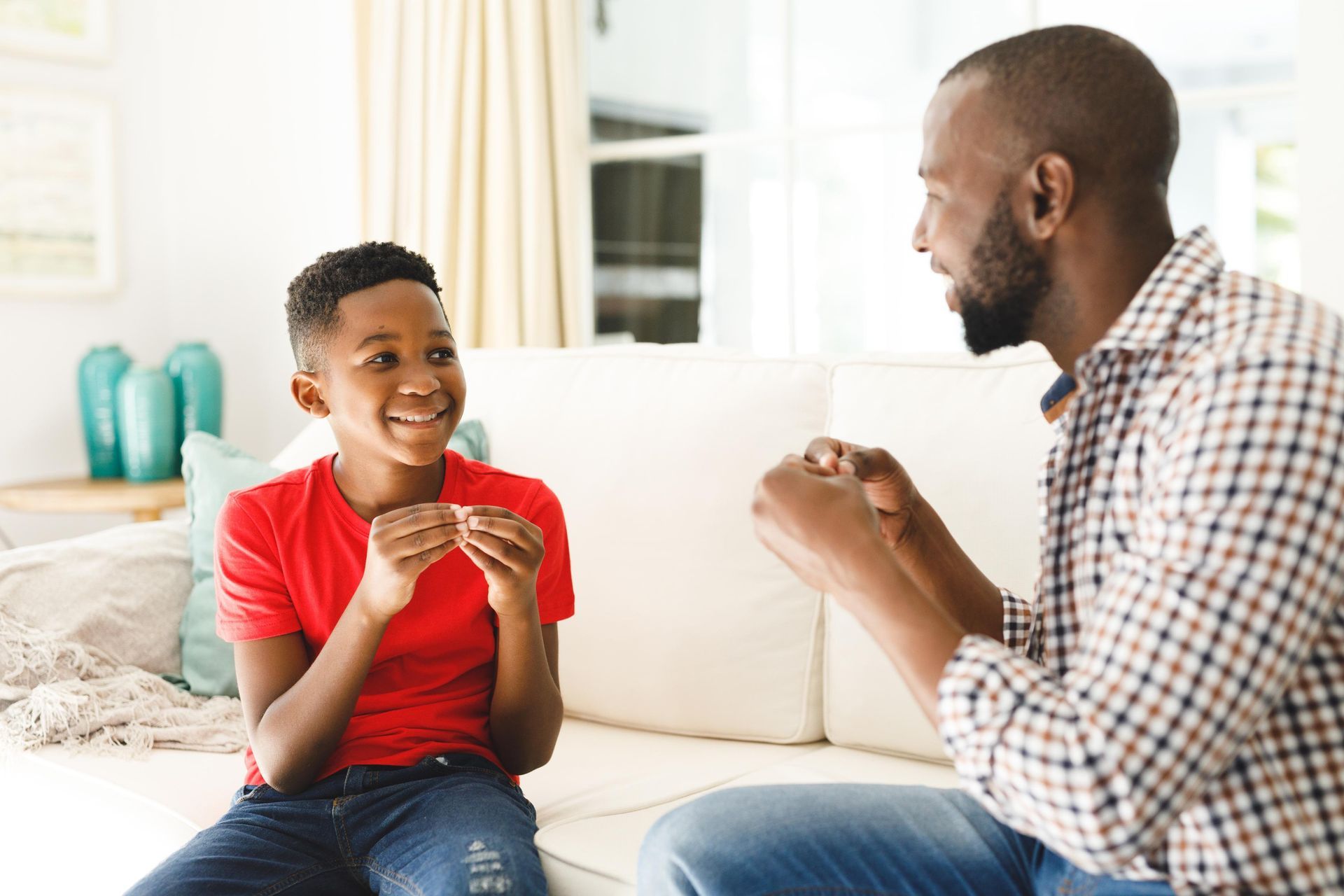 Man and boy on a couch communicating with sign language, boy smiles, interior.