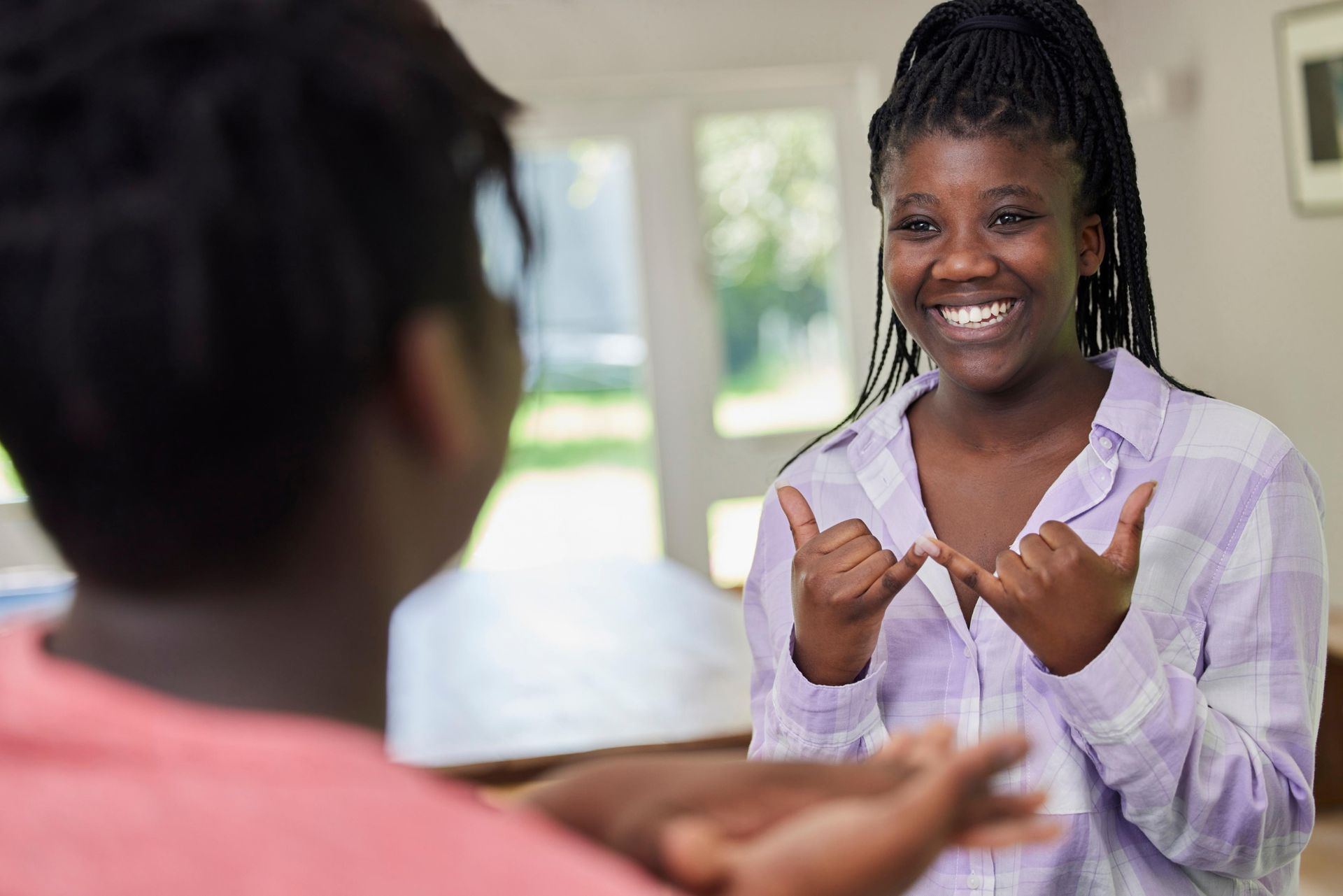 Two Black women conversing using sign language, one smiling, indoors.
