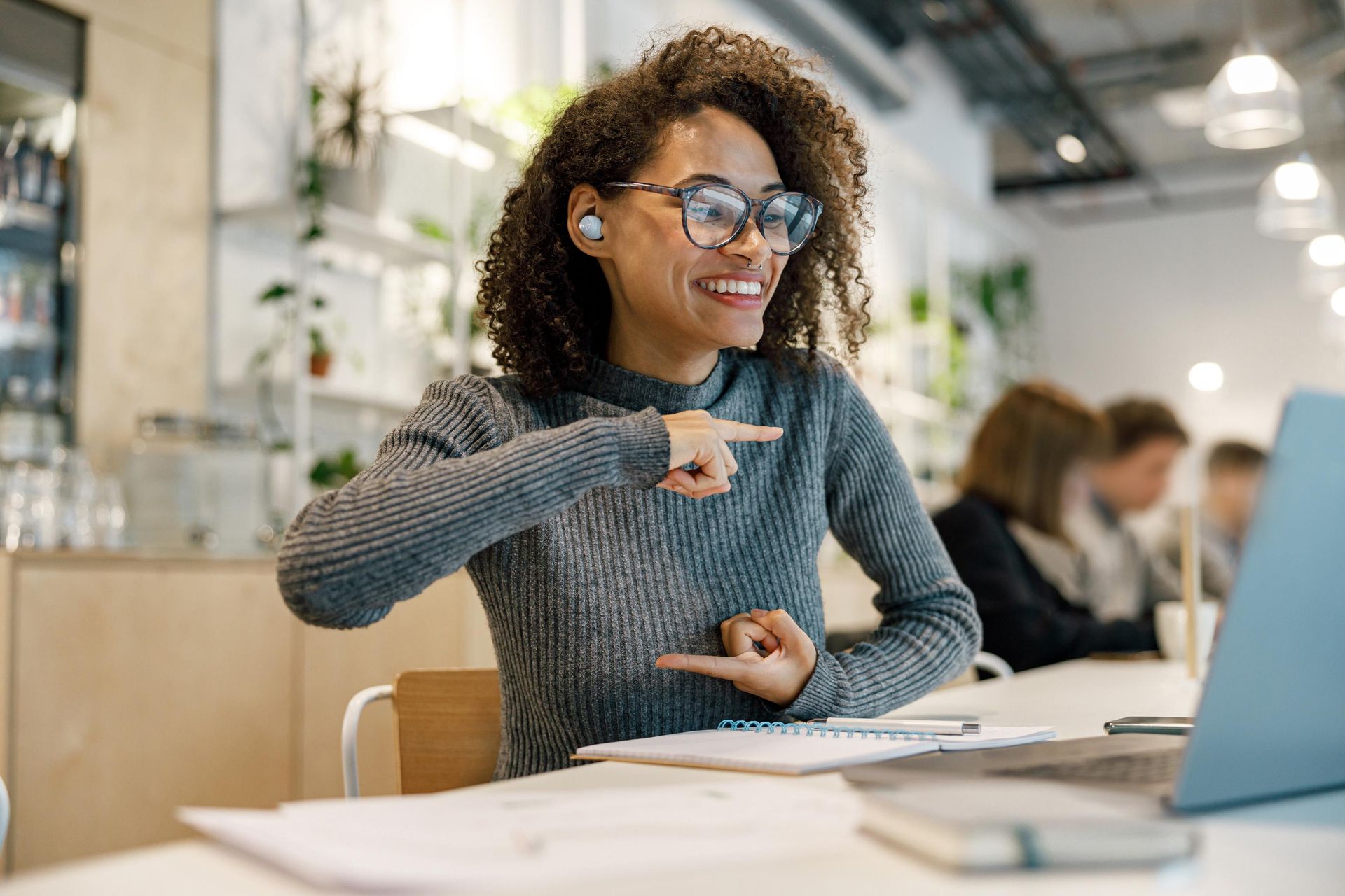 Woman with glasses using sign language, smiling, in a bright office.