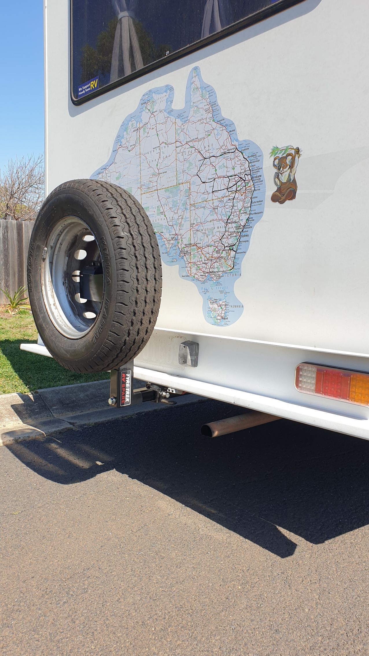 A camper with a spare tyre attached to the back of it is parked on the side of the road.