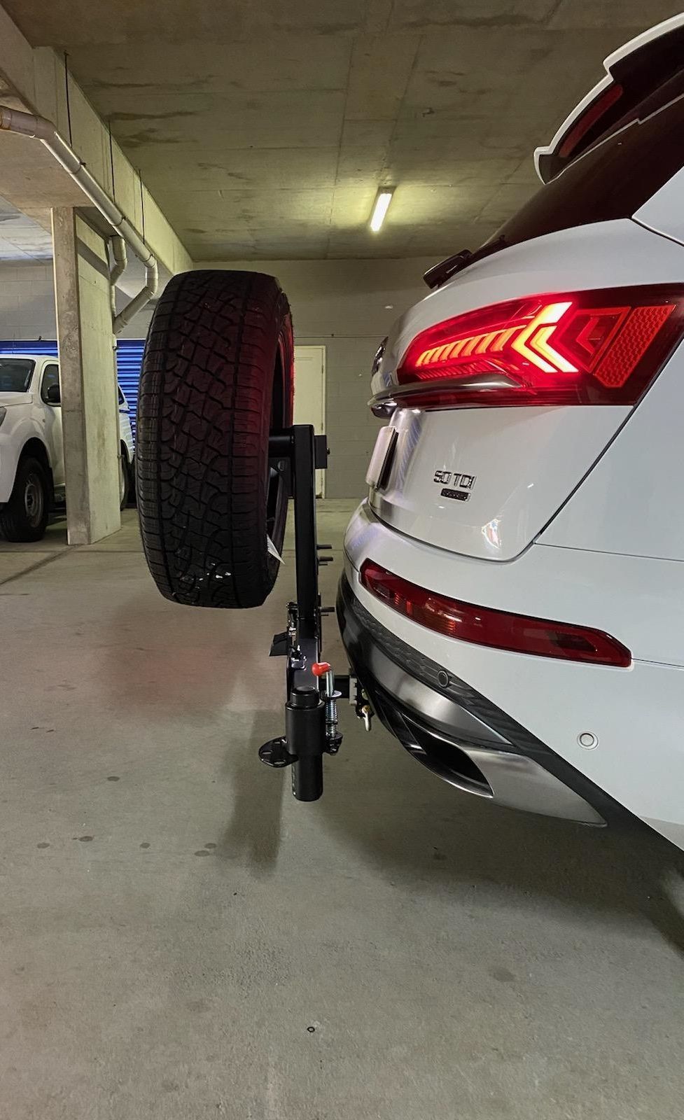 A white 4wd with a spare tyre attached to the back of it is parked in a garage.