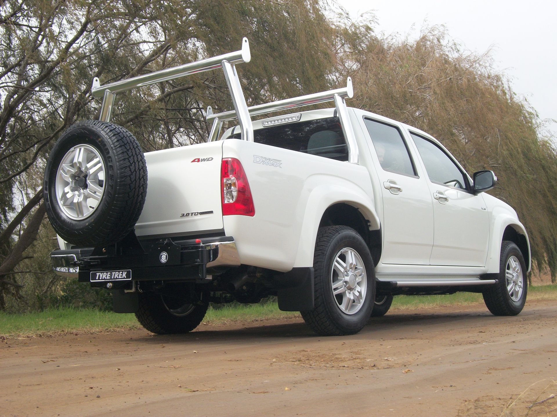 A white 4wd with a spare tyre on the back is parked on a dirt road.