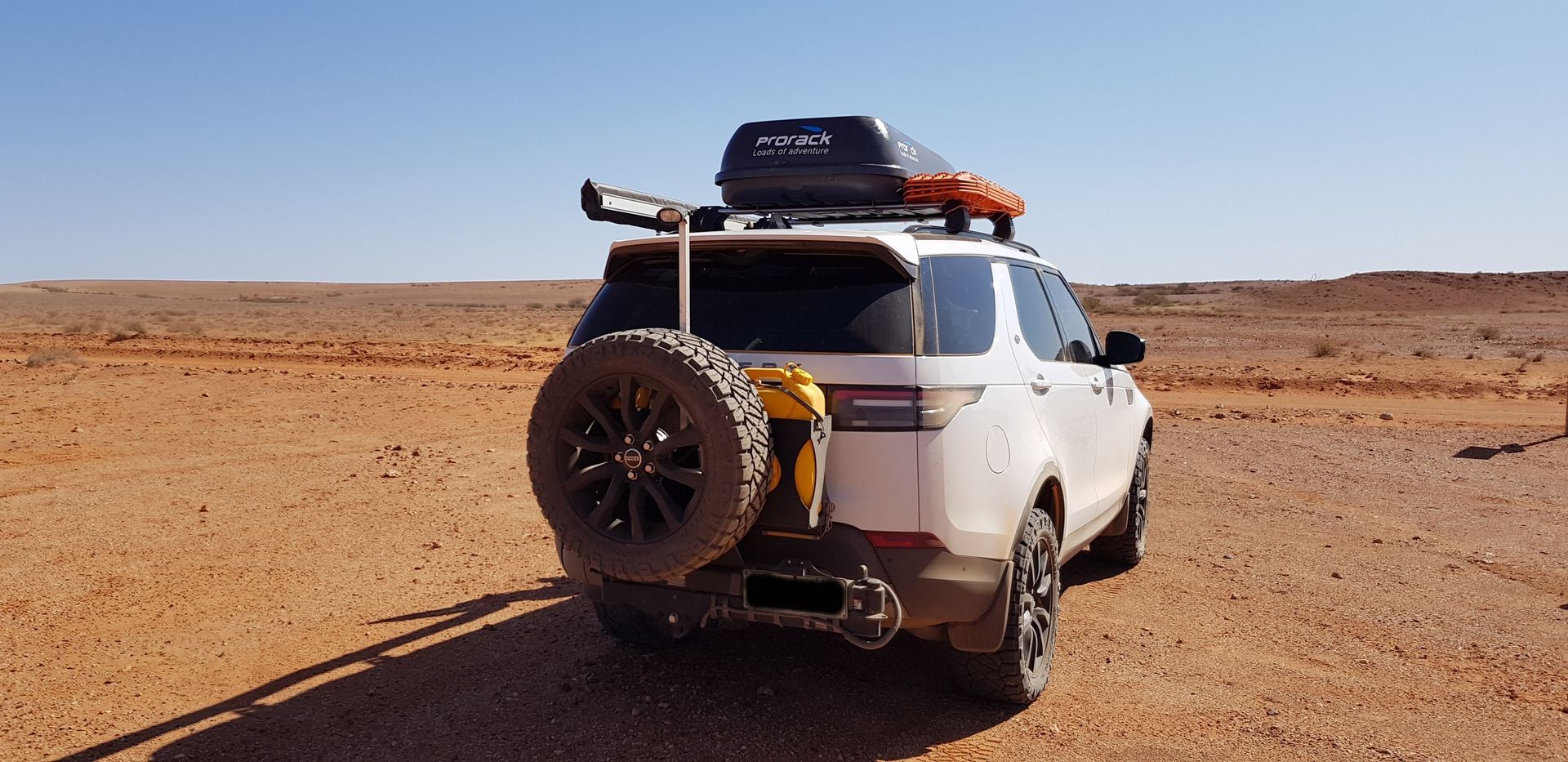 A white 4wd with a spare tyre on the back is parked in the australian outback.