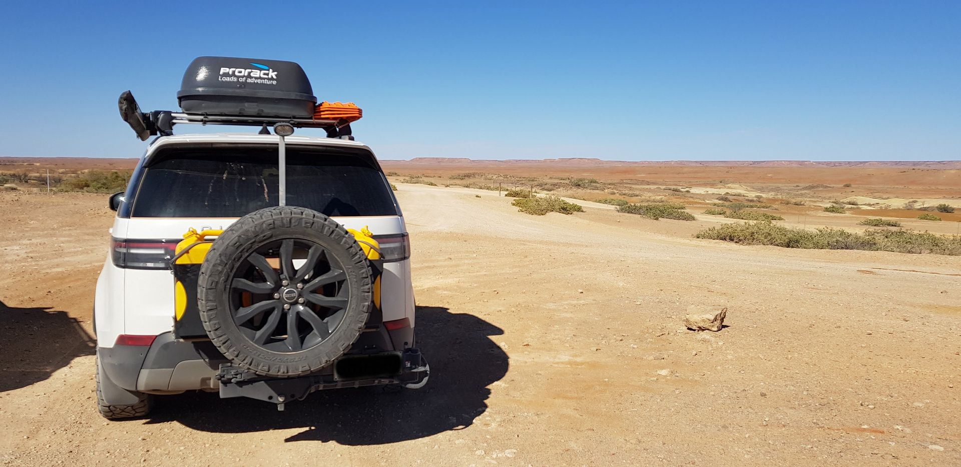 A white suv is parked on a dirt road in the desert.