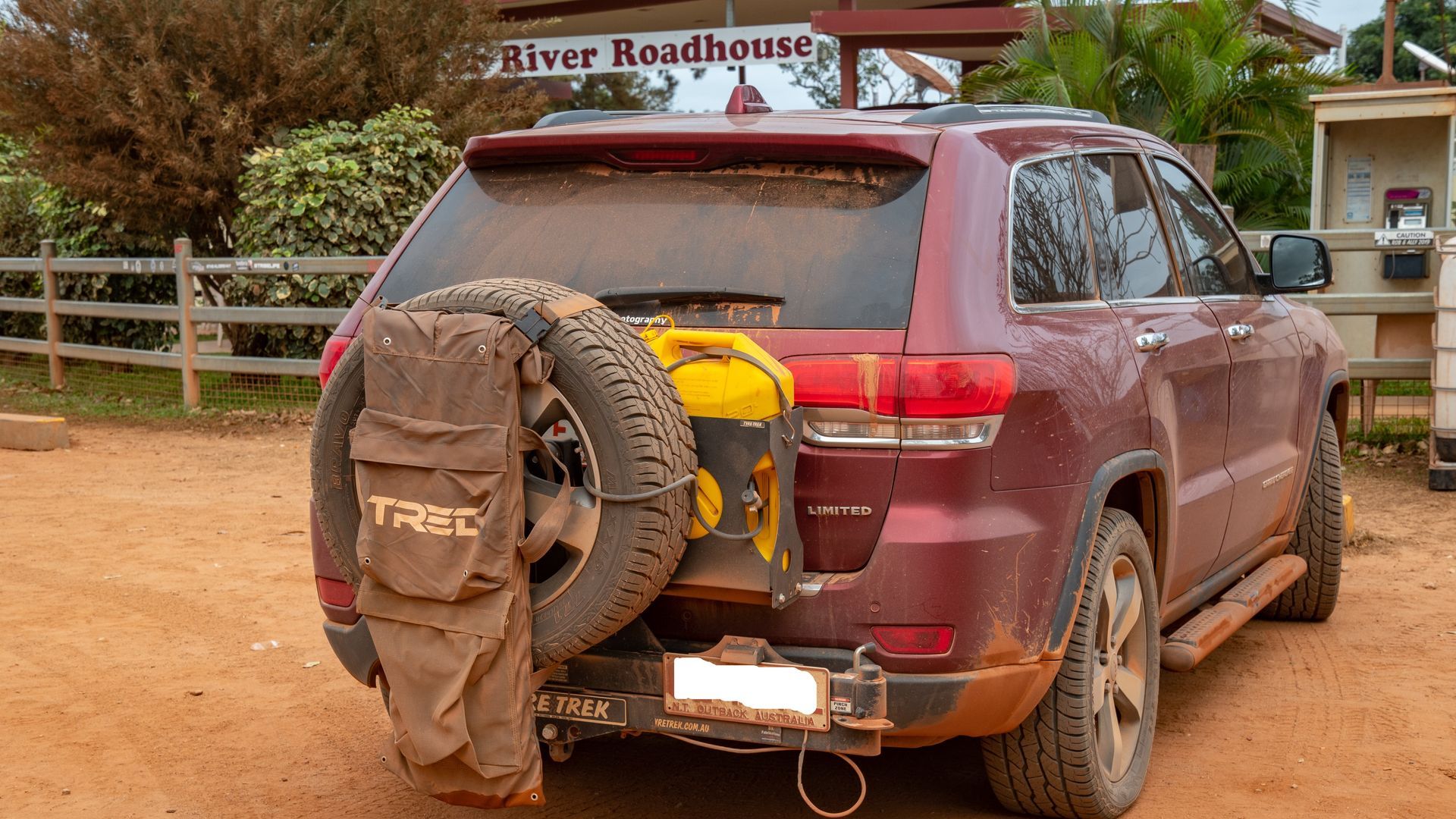 A red suv is parked in the dirt in front of a roadhouse.