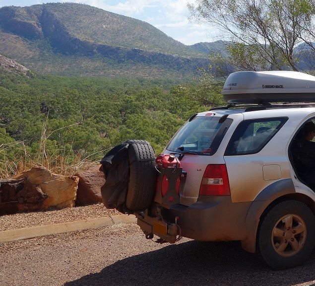 A 4wd with a roof box on top of it is parked by the side of the road in the australian bush.