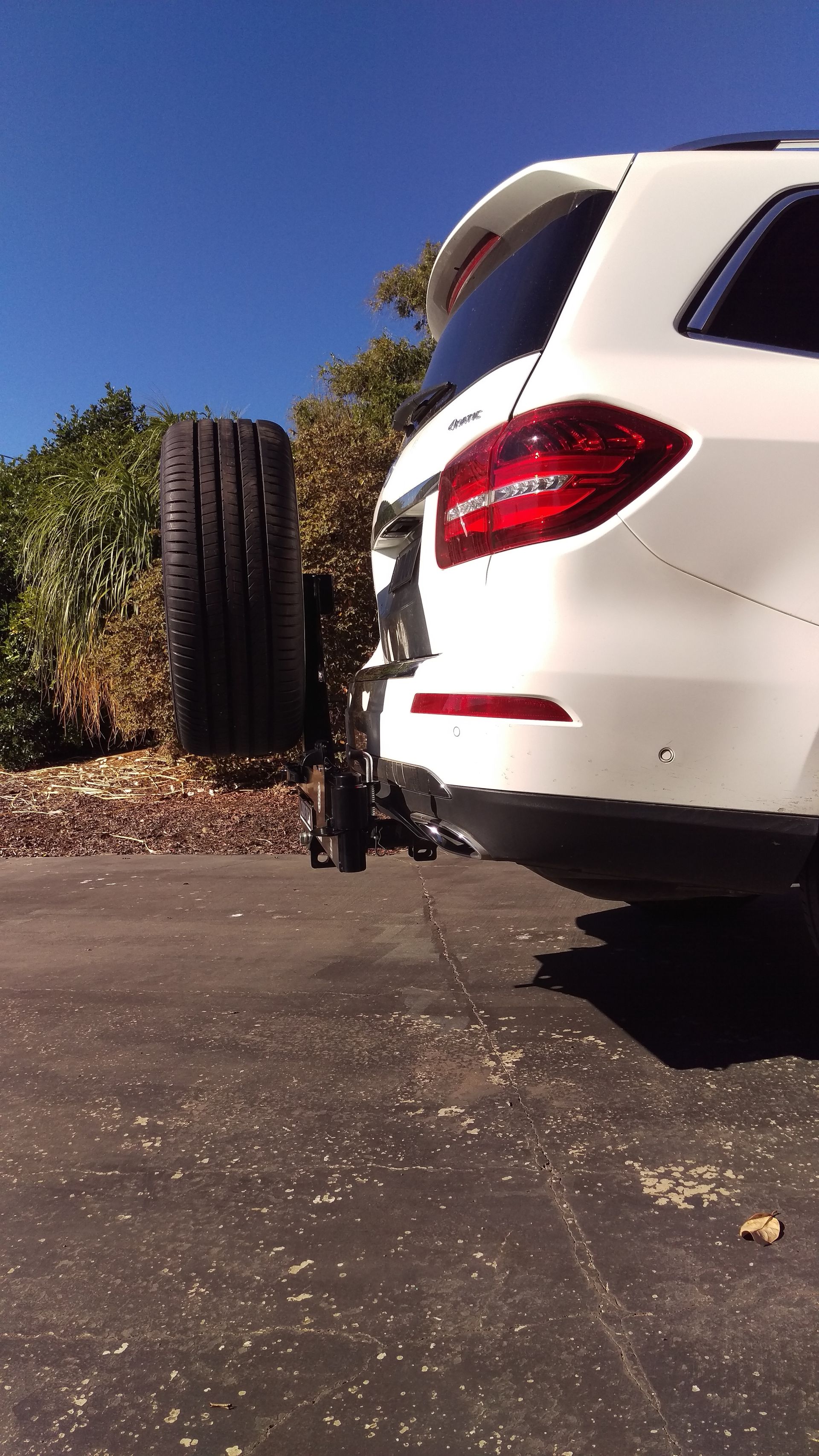 A white suv with a spare tyre on the back is parked on the side of the road.