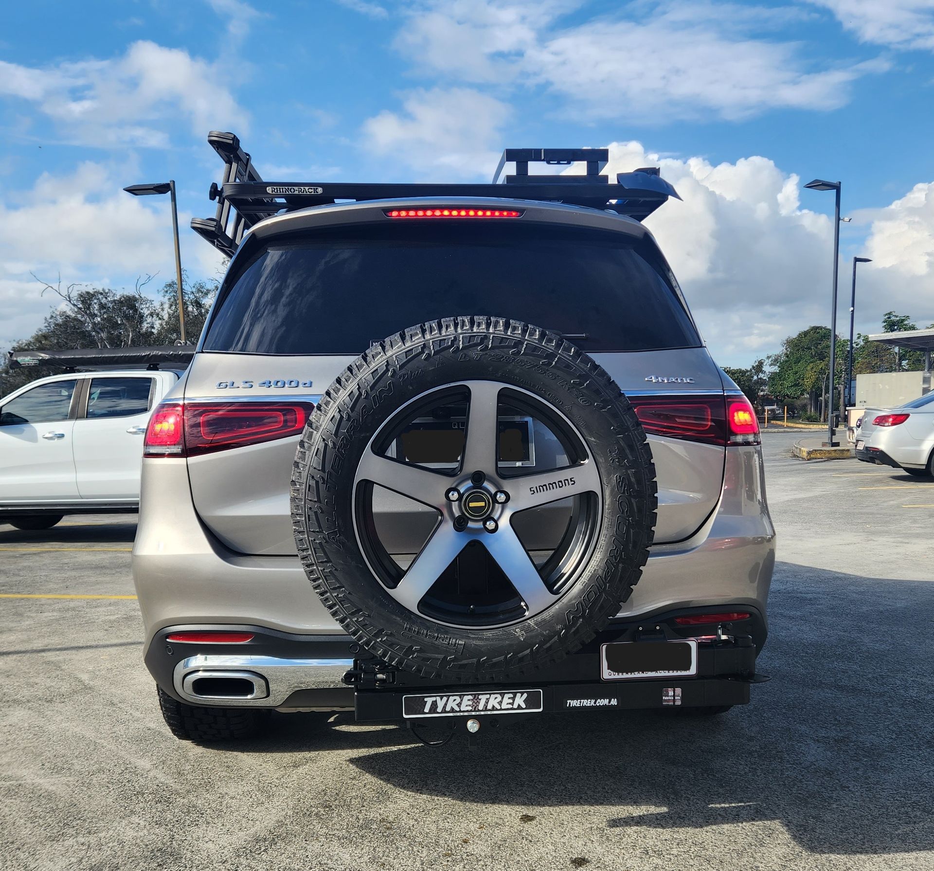 A silver suv with a spare tyre on the back is parked in a carpark.