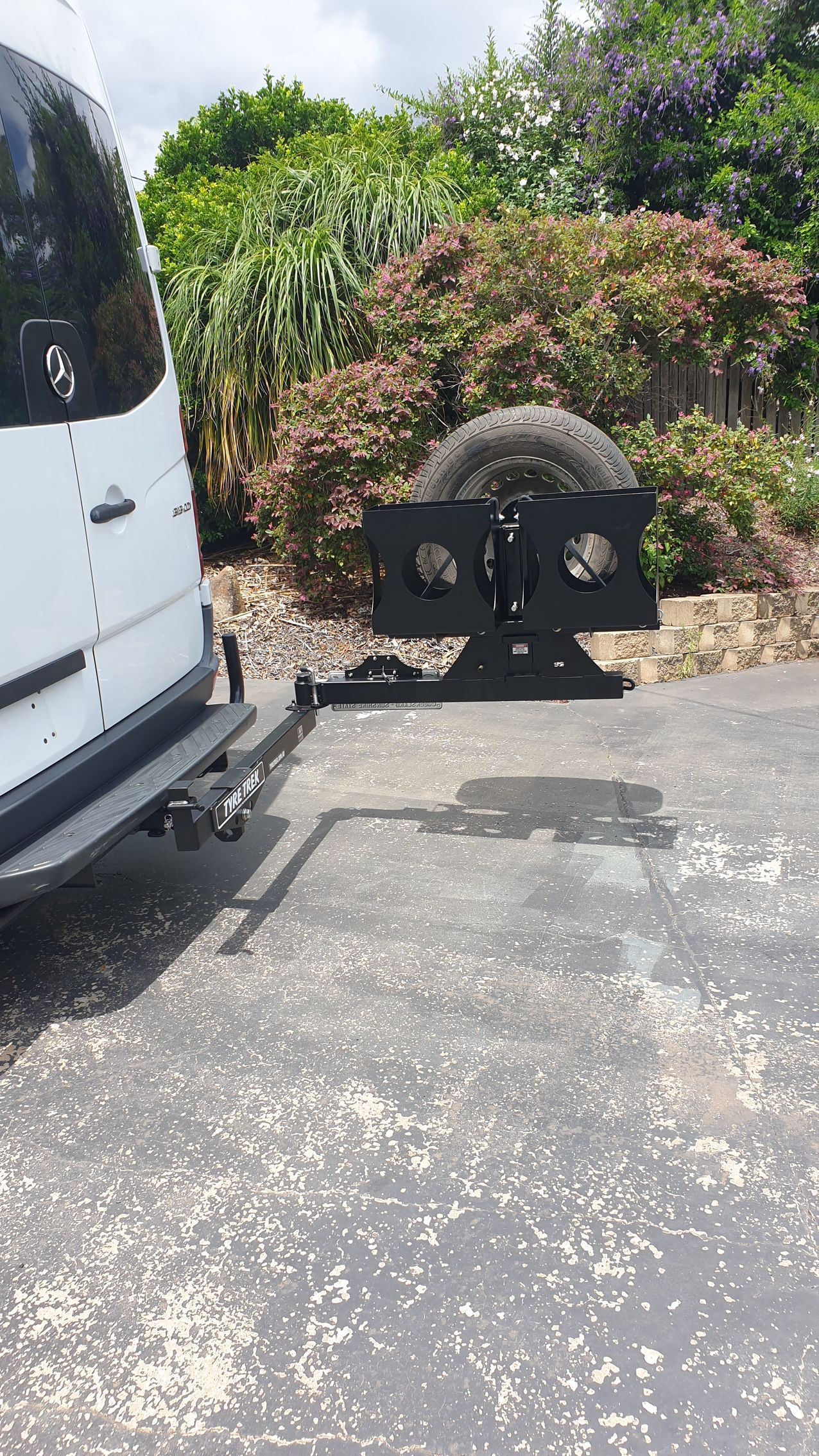 A white van is parked in a driveway with a a tyre rack attached.