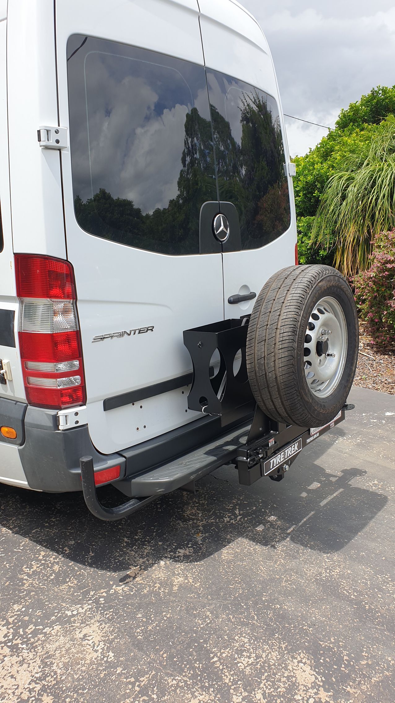 A white van with a spare tyre attached to the back is parked on the side of the road.
