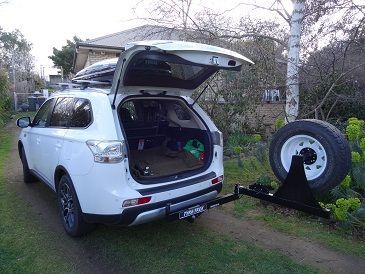 A white suv with its boot open and a tyre rack attached to it.