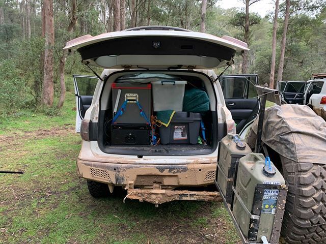 A car with the boot open is parked in the bush.